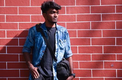 Young man looking away against brick wall