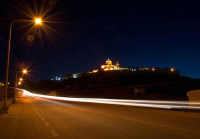 Illuminated light trails on road against sky at night