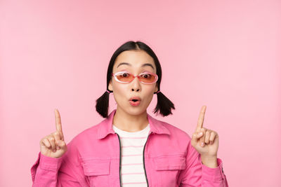 Portrait of young woman with arms raised against pink background