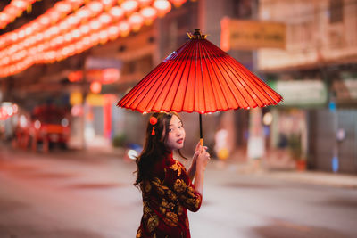 Portrait of woman with red umbrella standing against illuminated wall