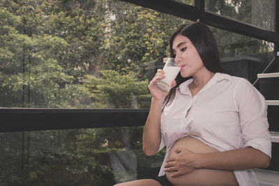 Pregnant woman drinking milk while sitting on steps at home