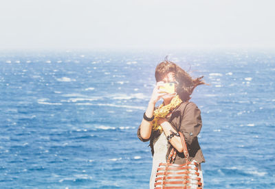 Woman photographing with camera against sea