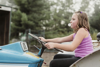 Girl blowing bubble gum while driving tractor in farm