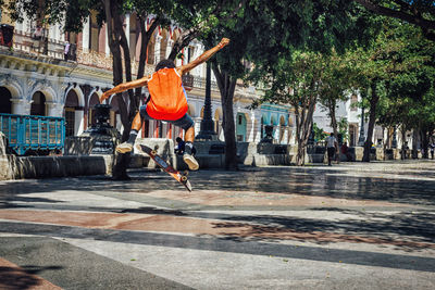 Rear view full length of man skateboarding on street in city during sunny day