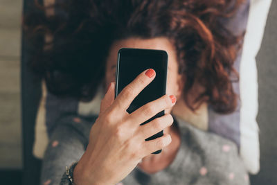 Woman holding mobile phone over face while lying on sofa