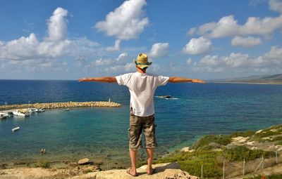 Rear view of man with arms outstretched looking at sea against sky