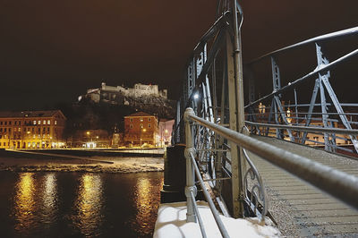 Illuminated buildings by river against sky in city at night