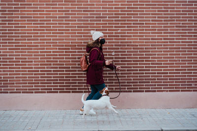 Woman with dog walking on footpath against wall