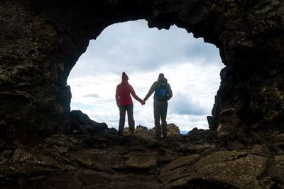 Rear view of couple standing on rock formation against sky