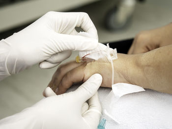 Cropped image of doctor removing medical equipment from patient hand in hospital