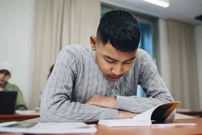 Teenage boy reading book while studying at table school