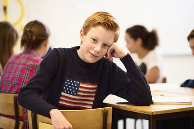 Portrait of confident schoolboy sitting at desk in classroom