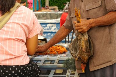 Midsection of man holding chicken while standing at market stall
