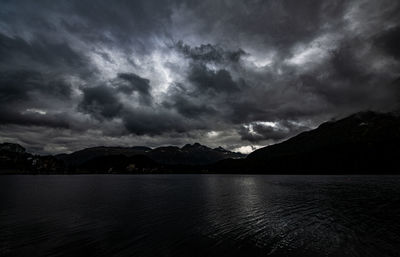 Scenic view of lake and mountains against storm clouds