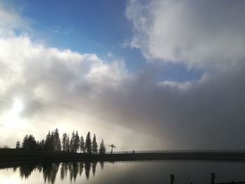 Low angle view of silhouette trees by lake against sky