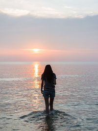 Rear view of woman standing on beach during sunset