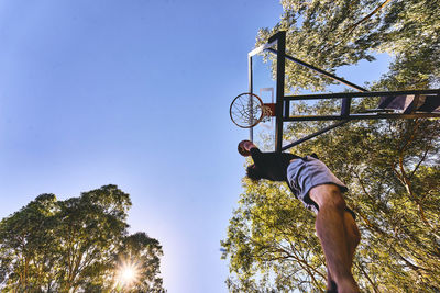 Low angle view of man putting ball in basketball hoop against clear sky