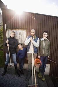 Portrait of confident family with gardening equipment standing against house