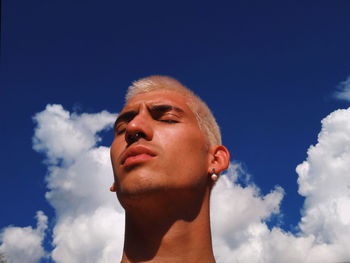 Low angle view of young man with eyes closed against sky