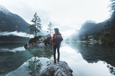 Rear view of woman standing on rock in lake against mountains and sky