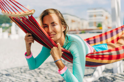 Young smiling tanned european woman relaxing in a hammock on the beach in summer.