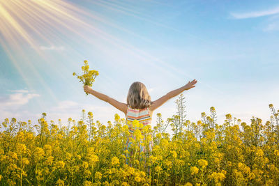 Rear view of woman standing amidst oilseed rape field against sky