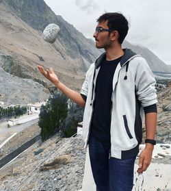 Young man catching rock while standing against mountain