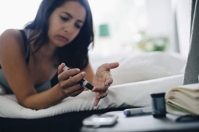 Woman checking blood sugar level while lying in bedroom