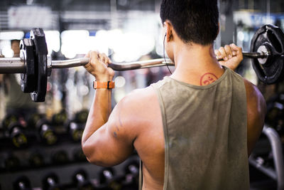 Rear view of muscular build man lifting barbell at gym