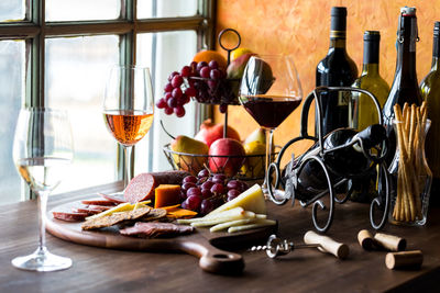 A rustic tabletop scene of gourmet wine and cheese, against a bright window.