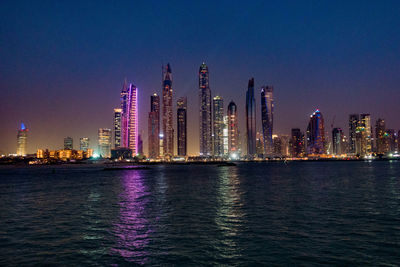 Illuminated cityscape by sea against sky at night