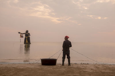 Rear view of men fishing in sea against sky