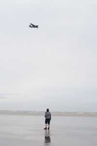 Rear view of man standing at beach against sky