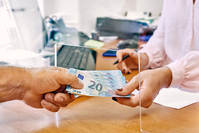 Social worker taking or giving euro money from client at office workplace with plexiglass separator.