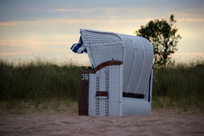 Beach chair on sand against sky during sunset