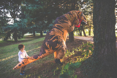 Boy playing with person wearing dinosaur costume in park