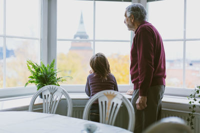 Senior man and great grandson looking through window at home