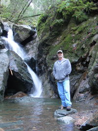 Portrait of young woman standing on rock against waterfall