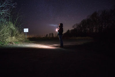 Person holding illuminated flashlight while standing on road at night