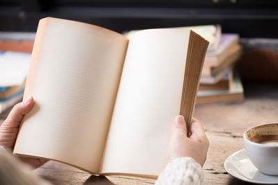 Cropped hands of woman holding book by coffee in cafe