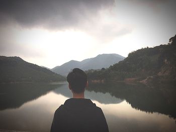 Rear view of man looking at lake against mountain