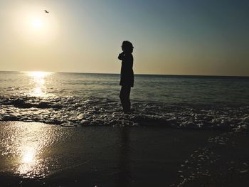 Silhouette man standing on beach against clear sky during sunset