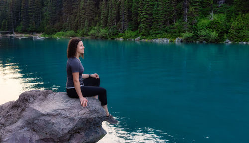 Side view of man sitting on rock by lake