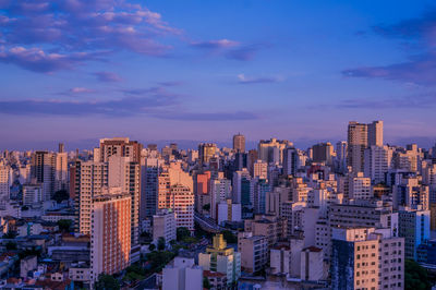 Aerial view of buildings in city against blue sky