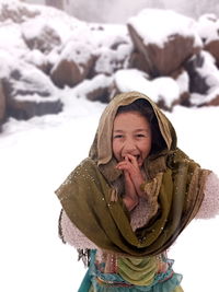 Portrait of smiling young woman sitting on snow covered field