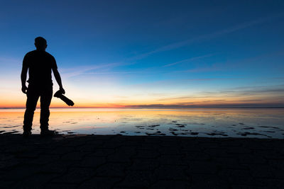Silhouette man standing on beach against sky during sunset