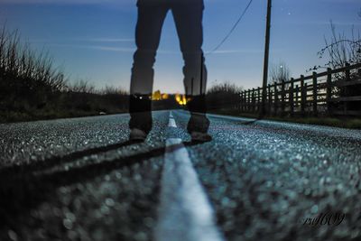 Low section of ghost standing on road against sky at sunset