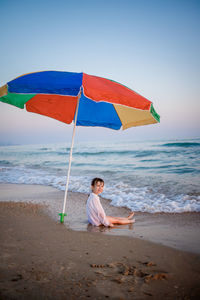 Boy sitting on beach by sea against sky