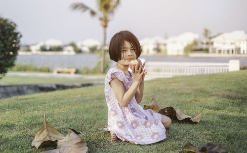 Portrait of girl holding apple while sitting on field