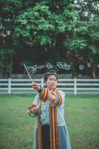 Woman in traditional clothing making bubbles while standing on field 